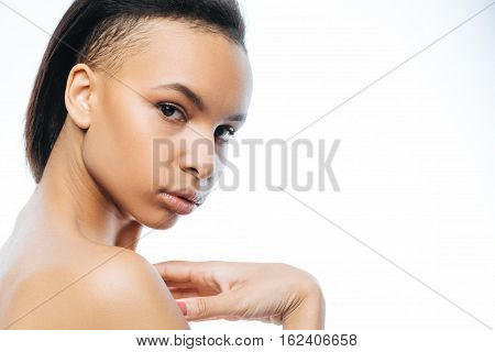 Charming glance. Beautiful passionate young Negroid woman touching her skin while standing against white background and expressing passion