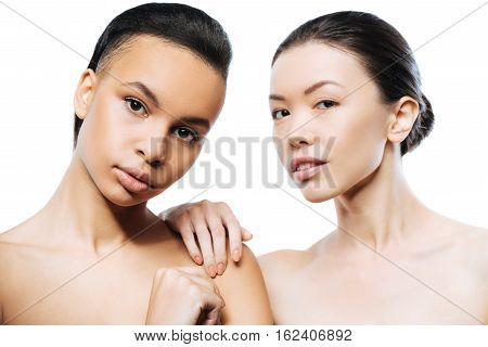 We enjoying modeling. Involved graceful passionate girls standing close to each other and expressing elegance while being isolated in white background
