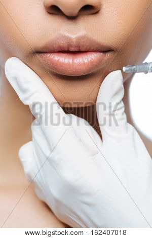 On the way of improvement. Pleasant involved young Negroid woman standing isolated in white background and expressing confidence while getting the injection in her lips