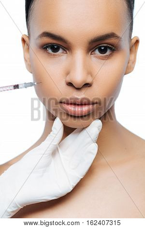 My appearance transformation. Decisive motionless young Negroid woman standing isolate in white background and expressing strength while getting the injection in her face