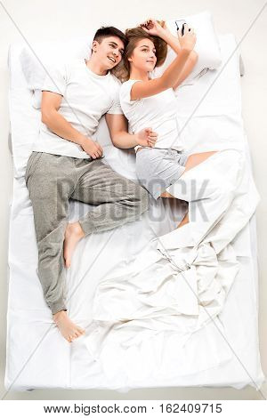 The young lovely couple lying in a bed with phone, love lconcept, top view