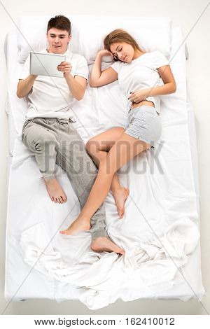 The young lovely couple lying in a white bed with laptop, love lconcept, top view