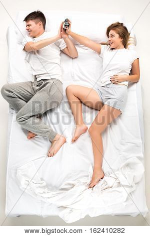 The young lovely couple lying in a white bed with alarm clock, love lconcept, top view