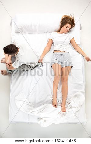 The young lovely couple lying in a white bed with alarm clock, love lconcept, top view