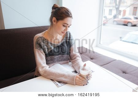 Photo of tenderless lady sitting in cafe near window holding glass of coffee. Look at coffee.