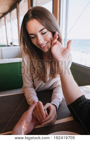 Vertical image of beauty woman sitting by the table on date in cafe near the sea and her man touching her cheek. First-person view