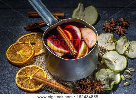 Small stewpot with mulled wine and cinnamon sticks, dry slice of oranges and apple, star anise on a dark table