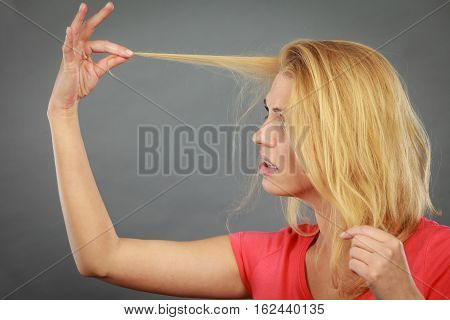 Haircare health problem concept. Unhappy sad woman looking at damaged split ends on her blonde hair