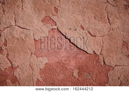 Distressed patchy red cement render faded by the sun