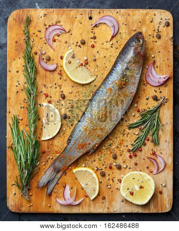 Fresh Grey Mullet Fish Lies On Light Wooden Cutting Board With Lemon Segments, Onion Slices, Rosemar