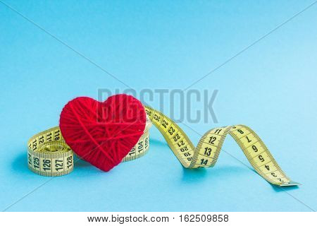 Red heart with yellow tape measure on blue background