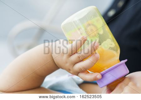 hand of baby holding orange juice bottle suck in embrace mother