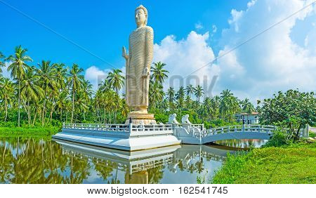 The Buddha Statue on the tiny island connected with the river bank by the small bridge guarded by two white lions Peraliya Sri Lanka.