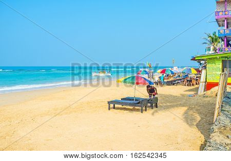 HIKKADUWA SRI LANKA - DECEMBER 5 2016: The comfortable sand beach with sun beds umbrellas cafes and restaurants for the tourist pleasure on December 5 in Hikkaduwa.