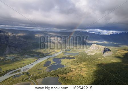 Spectacular sunlight on autumn landscape and rainbow in the rain clouds