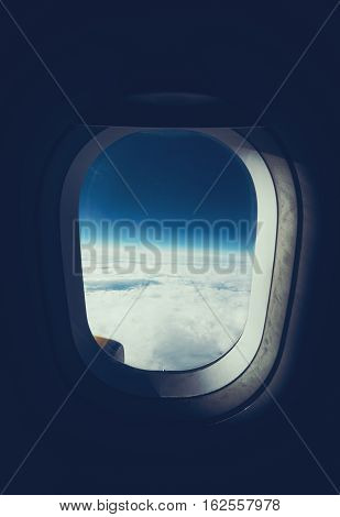 View through airplane porthole of horizon clouds and dark sky