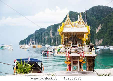 Traditional spirit house in Thailand (san phra phum) against turquoise sea water, ships and mountains.Phi-Phi