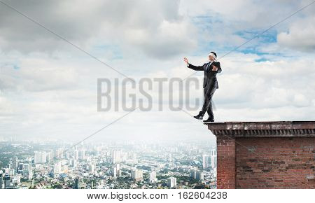 Businessman with blindfolder on eyes walking on building top