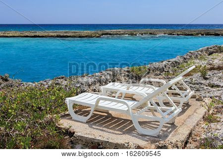 two chaise-lounges on the coral beach of the Caribbean sea