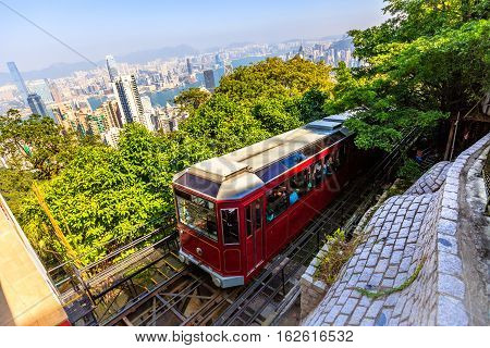 The popular red Peak Tram as he arrives at the terminus of Victoria Peak, the highest peak of Hong Kong island, with panoramic city skyline in background. Sunny day.