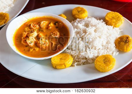 Coconut shrimp stew (encocado) served in white dish with rice and fried plantains