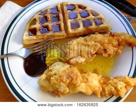Half of a waffle covered in syrup, with two fried chicken fingers.