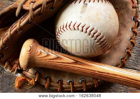 A close up image of an old used baseball glove and bat.
