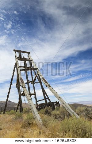 Old mining head frame in the Nevada Desert under blue sky with clouds.