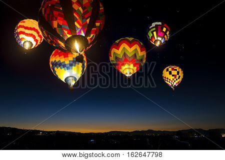Colorful hot air balloons at dawn lit up in the sky.