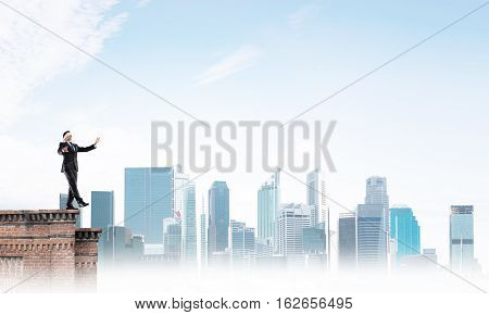 Businessman with blindfolder on eyes walking on building top