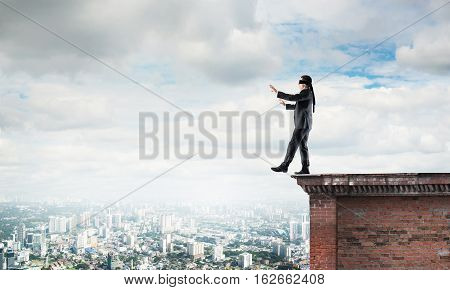 Businessman with blindfolder on eyes walking on building top