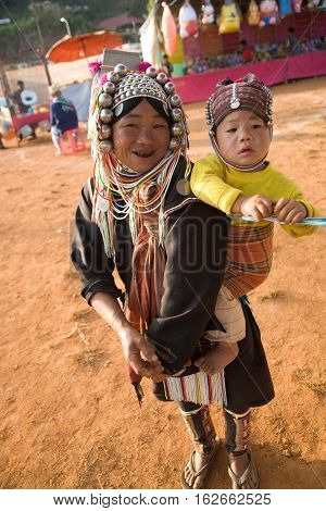 Mae Salong, Thailand - January 28, 2008 : 
In the mountains of northern Thailand. An woman from the Akha ethnic group carries her baby behind her back. To save her money Akha women sew silver coins on headdress.
