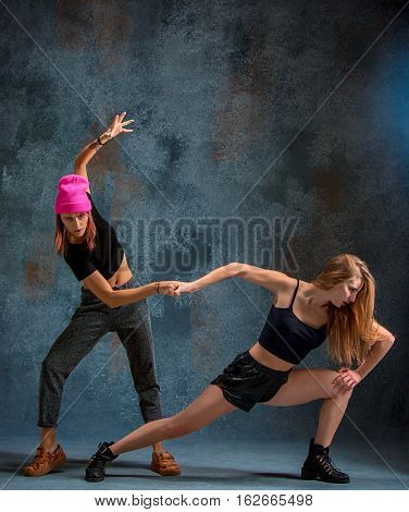The two attractive girls dancing twerk iat the blue studio background
