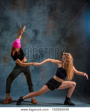 The two attractive girls dancing twerk iat the blue studio background