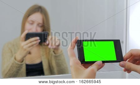 Woman sitting in front of a mirror and using horizontal smartphone with green screen. Close up shot of woman's hands with mobile Close up shot of woman's hands with mobile