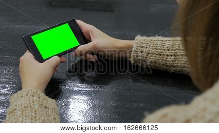 Woman looking at smartphone with green screen. Close up shot of woman's hands with mobile