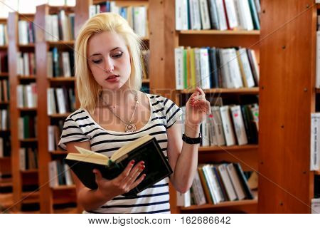 Blonde girl reading book in front of full bookshelves