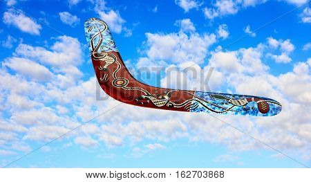 Multicolored australian boomerang flies in sky against of pure white clouds.