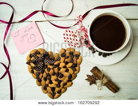 White plate in the form of seashells with coffee beans, cinnamon sticks and star anise, a festive tablecloth and cup with saucer on a dark wooden background.