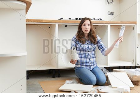 Frustrated Woman With Self Assembly Furniture In Kitchen