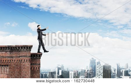 Businessman with blindfolder on eyes walking on building top