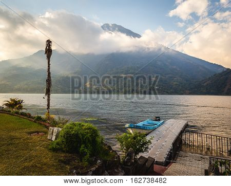 View on beach at Lake Atitlan, Guatemala, Central America. Clouds and blue sky over volcanic mountain. Dock in foreground.