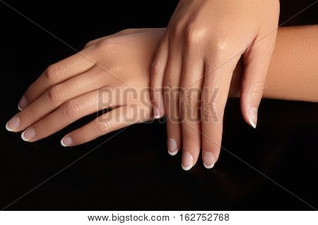 Beautiful female arms with ideal french manicure on black background. Care about female hands healthy soft skin. Spa and cosmetics. Beauty care. Close-up of beautiful famele fingers with nails polish