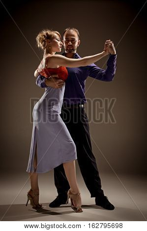 A man and a woman dancing argentinian tango on gray studio background