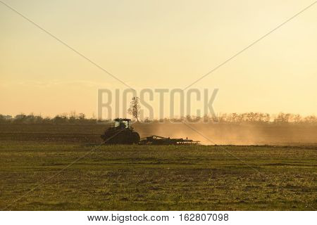 Tractor At Sunset Plow Plow A Field. Tilling The Soil In The Fall After Harvest. The End Of The Seas