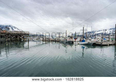 View of fishing boats moored at the port of Seward and snow covered mountains behind Alaska