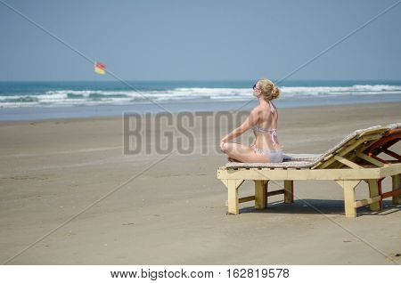 blonde girl in a bikini sitting on a sun lounger on the ocean