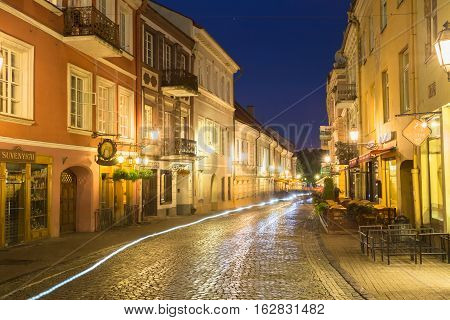 Vilnius, Lithuania - July 8, 2016: View Of Deserted Pilies Street Of Old Town In Bright Evening Illumination With White Motion Blur Effect On Cobbled Road, Famous Landmark Under Summer Night Blue Sky.