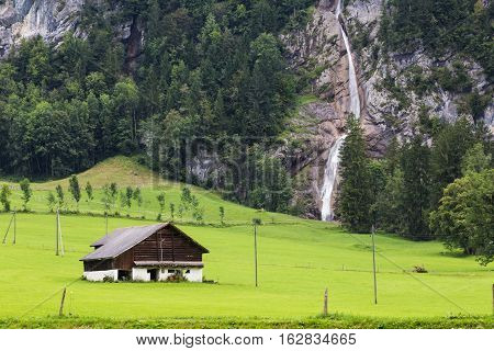 Alpine mountain landscape - small house on a green meadow against the background of a waterfall. Switzerland. Canton Glarus