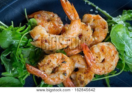 close up with fresh fried shirmps with arugula on a black plate